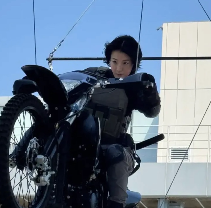 Cena de ação sendo gravada, com uma moto suspensa em equipamento de filmagem
