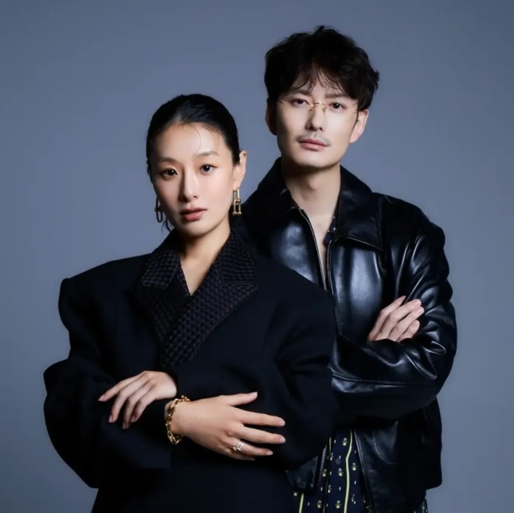 Hyunri e Machida Keita juntos, os dois de preto, em foto de estúdio