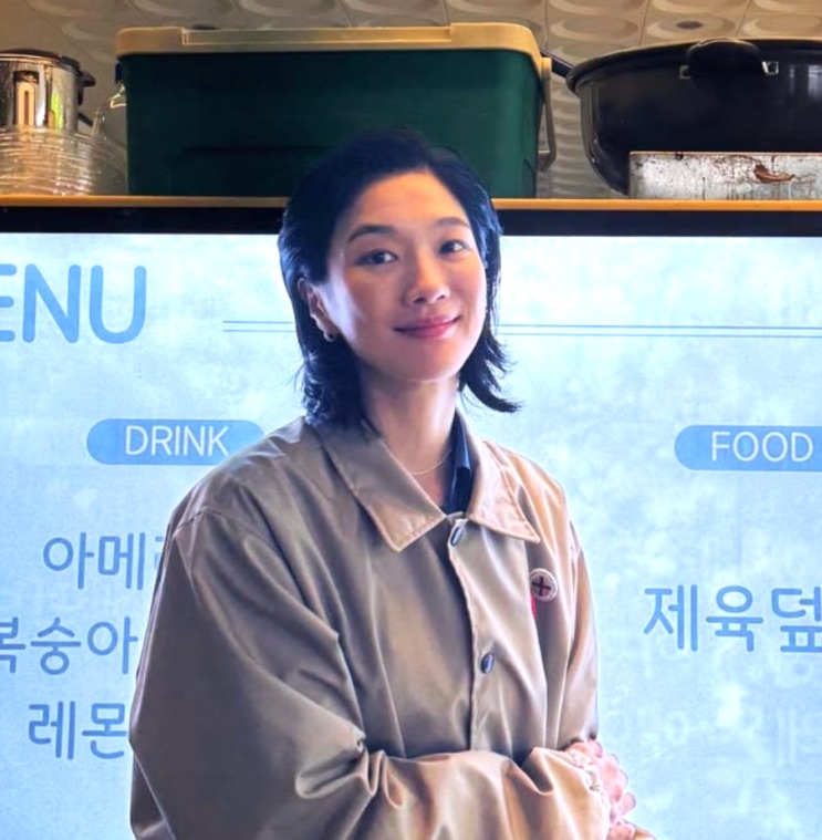 Jung Yun-ha de casaco bege dentro de uma lanchonete, sorrindo