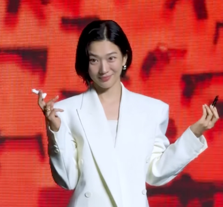 Jung Yun-ha de terno branco abrindo os braços diante de um fundo vermelho