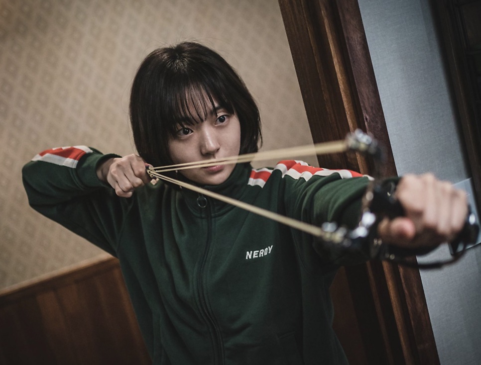 Jeong Ji-an de agasalho verde, mirando com um estilingue esticado