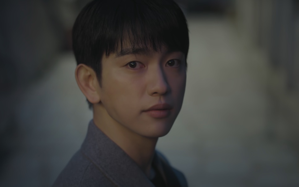 O Ho-su de casaco cinza, olhando para a frente com os olhos marejados