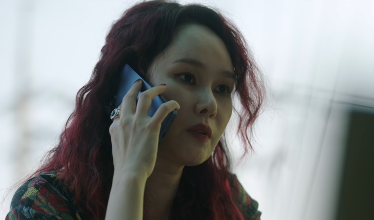 Jo Mi-yeon de cabelo ruivo, falando ao celular perto de uma janela