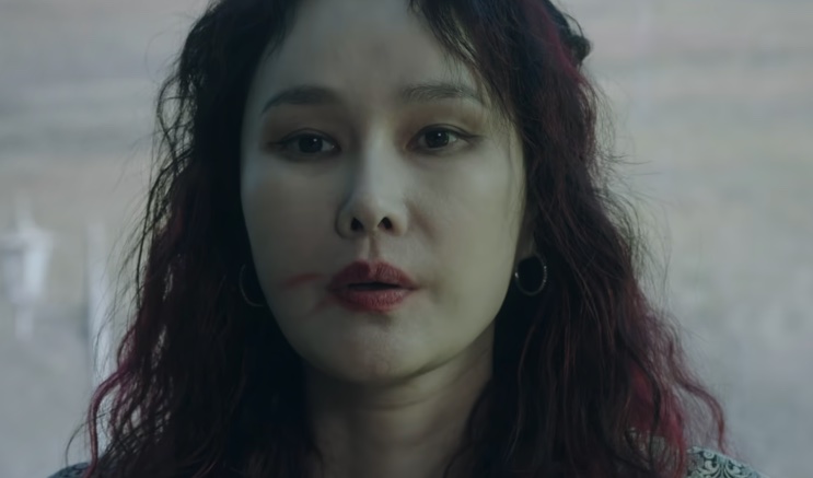 Close de Jo Mi-yeon de batom escuro, falando em um ambiente com pouca luz