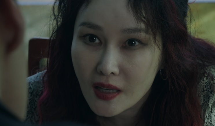 Jo Mi-yeon falando com alguém sentada, em um ambiente com luz baixa