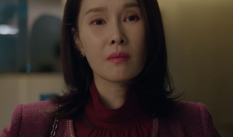 Baek Mi-hee de tricô vinho, olhando para a frente em um ambiente escuro