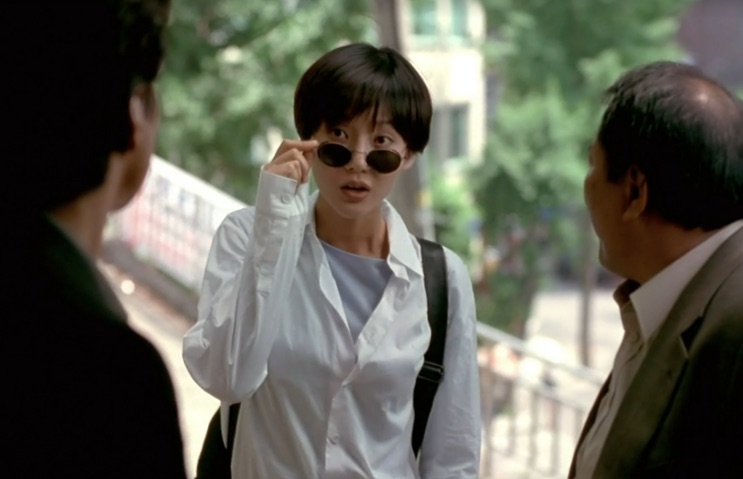 Yum Jung-ah de óculos escuros redondos e camisa branca, na rua