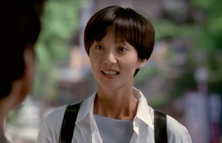 Yum Jung-ah de camisa branca e suspensórios, olhando de lado