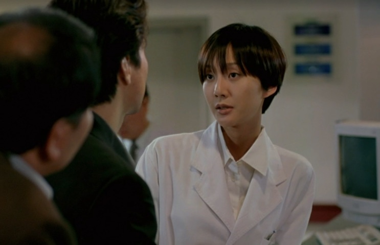 Yum Jung-ah de jaleco branco conversando com dois homens num corredor